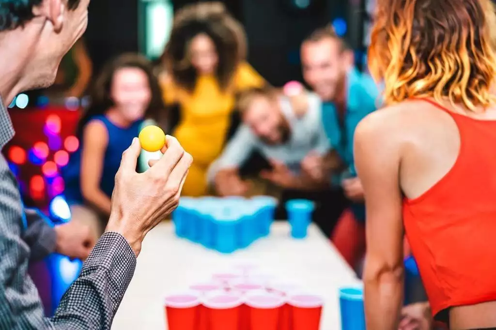 Un homme fait le geste de lancer la balle dans les gobelets de son rival lors d'une partie de beer pong pendant une fête.