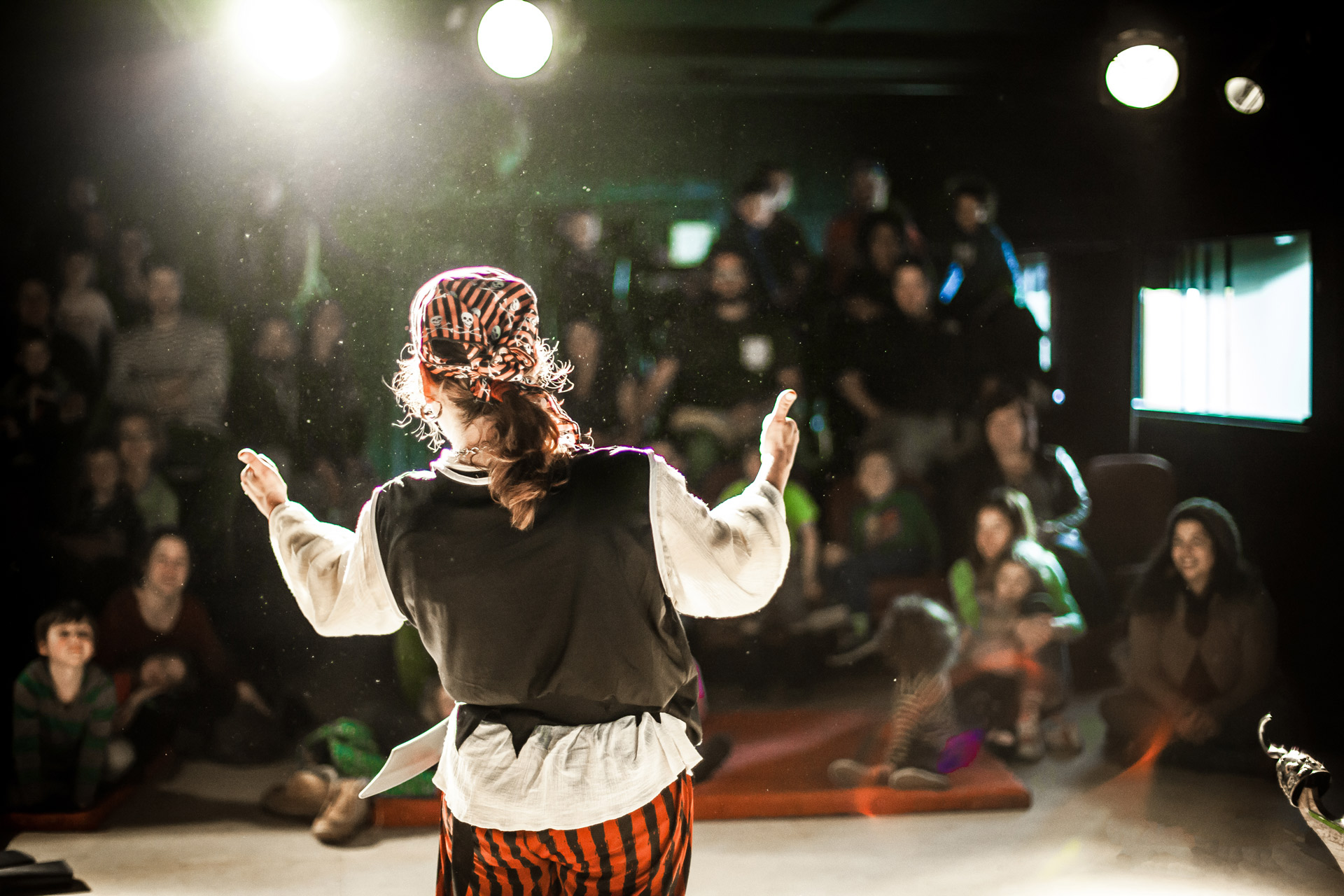 Un artiste de spectacle est vu de dos, avec une mise au point sélective, habillé en pirate sur scène pendant un numéro de comédie, avec un public flou à l'arrière.